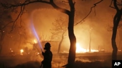 FILE - In this July 23, 2018 photo, a firefighter sprays water on the fire in the town of Mati, east of Athens. The fire killed 103 people in Greece's worst fire disaster in the nation's history. 