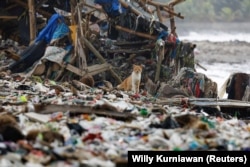 Seekor kucing terlihat di antara sampah yang sebagian besar berupa sampah plastik dan rumah tangga, di sebuah pantai di perkampungan nelayan Teluk, Pandeglang, Banten, 15 Maret 2024. (Foto: REUTERS /Willy Kurniawan)