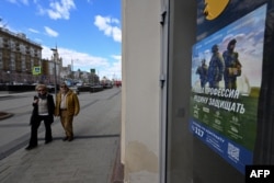 Plakat koji promoviše ugovornu vojnu službu i natpis "Naš posao, branimo otadžbinu" krasi vrata prodavnice, sa ambasadom SAD sa leve strane, u centru Moskve 22. aprila 2023.