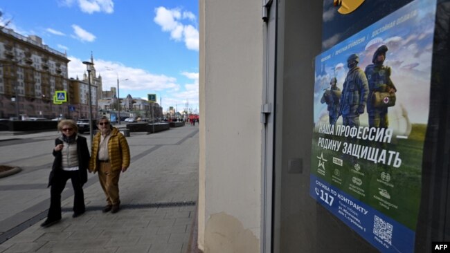 A poster promoting contract army service and reading "Our job, defending the homeland" adorns the door of a shop, with the U.S. embassy seen on the left, in central Moscow on April 22, 2023.
