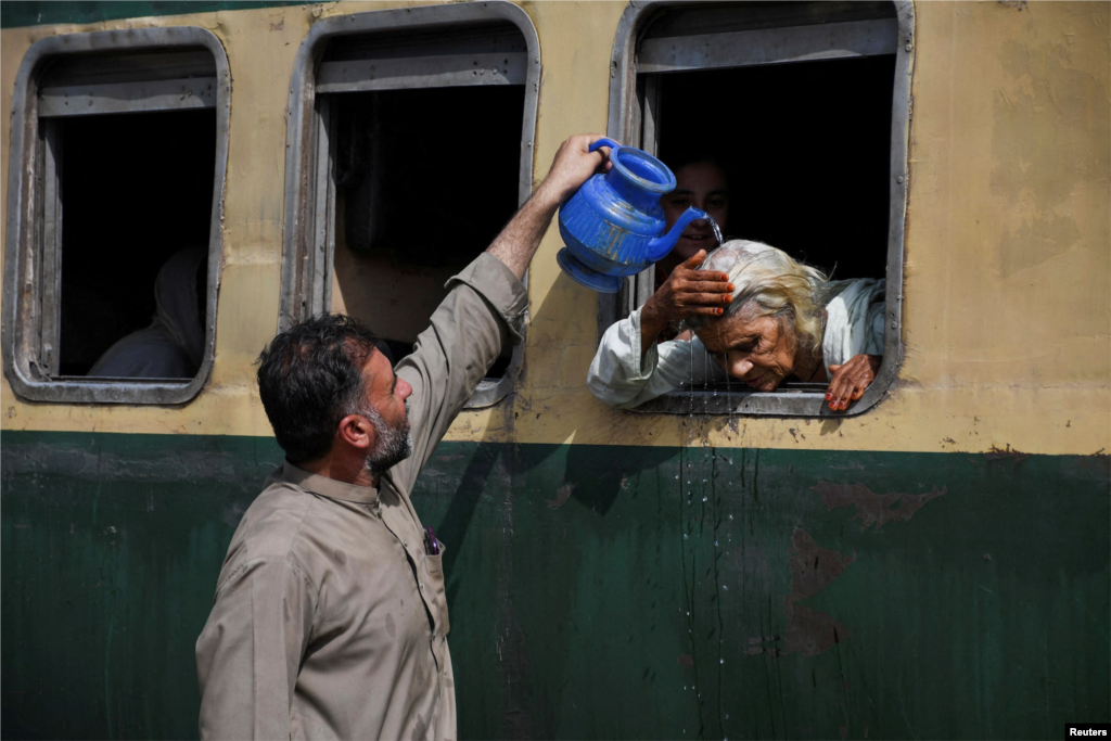 زنی که در ایستگاه راه آهن حیدرآباد در پاکستان از پنجره قطار به بیرون خم شده است، تا با دریافت کمی آب خنک شود