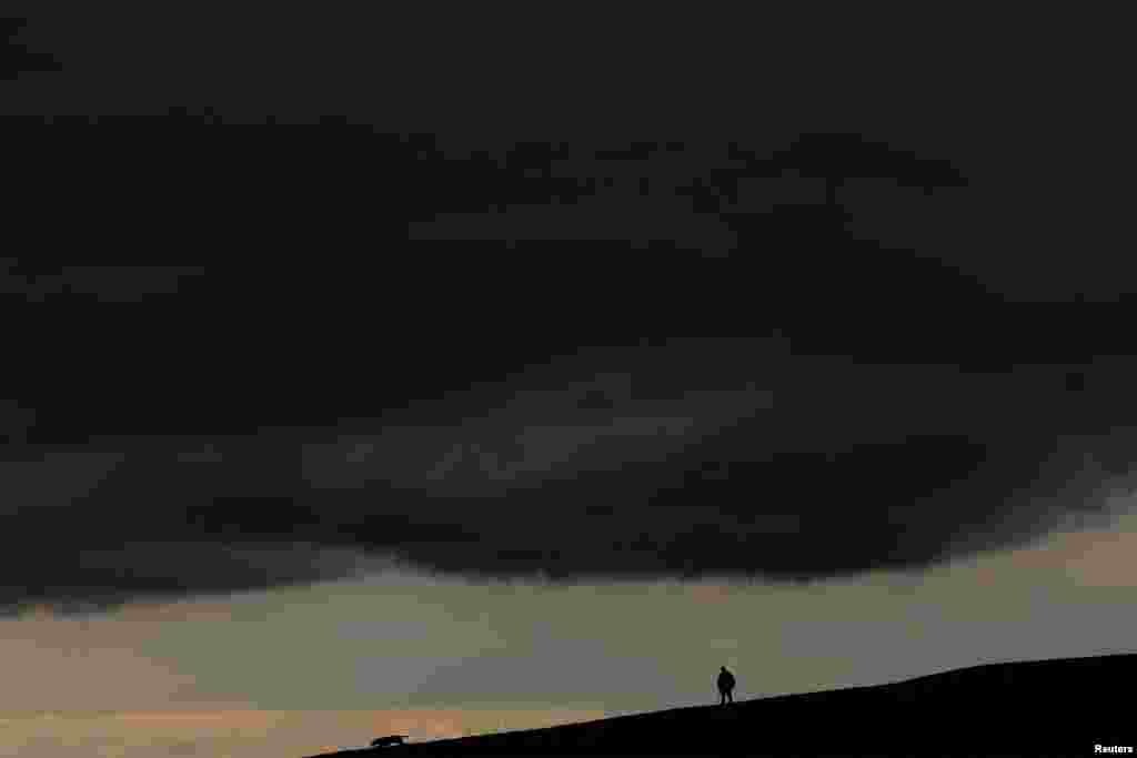 A man walks his dog under storm clouds on the Curragh race track, in Newbridge, Ireland, Aug. 16, 2023.