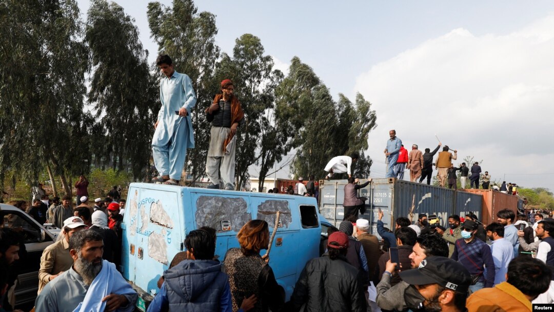 Supporters of former Pakistani Prime Minister Imran Khan climb on shipping containers, placed to block the road, during a clash outside the federal judicial complex in Islamabad, March 18, 2023.
