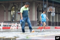 Roy Quiroz y su esposa, Minda, cruzan una sección inundada de The Strand cerca de Kempner Street mientras llueve el miércoles 19 de junio de 2024, en Galveston, Texas.