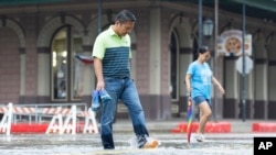 Roy Quiroz and his wife, Minda, cross a flooded section of The Strand near Kempner Street as rain falls in Galveston, Texas, June 19, 2024. Tropical Storm Alberto has formed in the southwestern Gulf of Mexico, the first named storm of the hurricane season.