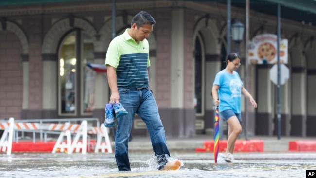 Roy Quiroz and his wife, Minda, cross a flooded section of The Strand near Kempner Street as rain falls in Galveston, Texas, June 19, 2024. Tropical Storm Alberto has formed in the southwestern Gulf of Mexico, the first named storm of the hurricane season.