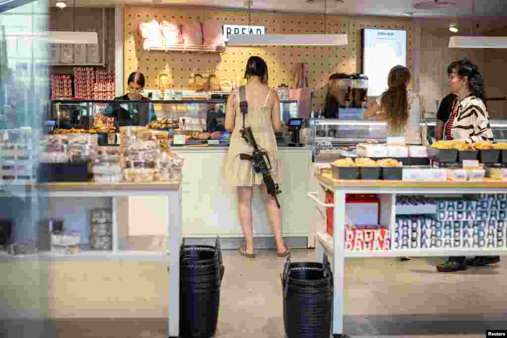 A woman with a rifle shops in a bakery in Tel Aviv, Israel, June 4, 2024.