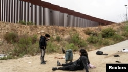 Asylum-seeking migrants from Turkey lay on the ground as they suffer from leg injuries after jumping down from the top of the border wall to cross into the U.S. from Mexico as seen from Tijuana, Mexico, June 8, 2024. 