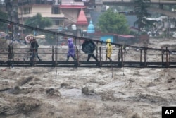 FILE - People walk through a bridge across River Beas swollen due to heavy rains in Kullu District, Himachal Pradesh, India, July 10, 2023.