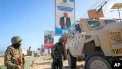 FILE - Ugandan peacekeepers with the African Transition Mission in Somalia (ATMIS) stand next to their armored vehicle on a street in Mogadishu, May 10, 2022.