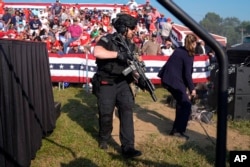 U.S. Secret Service agents surround the stage as other agents cover Republican presidential candidate former President Donald Trump at a campaign rally, July 13, 2024, in Butler, Pennsylvania.