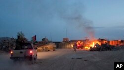 FILE - A pickup truck passes parked U.S. armored military vehicles as smoke rises from a fire in a trash burn pit at Forward Operating Base Caferetta Nawzad, Helmand province, Afghanistan, April 28, 2011.