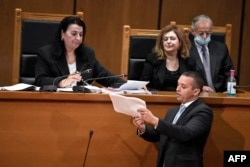 FILE - Ilias Kasidiaris, former Golden Dawn MP and spokesman, who was handed a sentence of 13 years imprisonment, presents documents to presiding judge Maria Lepenioti at the appeals court in Athens, Oct. 21, 2020.