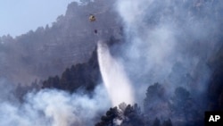 Sebuah helikopter tampak berusaha memadamkan kobaran api yang melalap area hutan di Montanejos, Castellon de la Plana, Spanyol, pada 26 Maret 2023. (Foto: AP/Alberto Saiz)