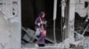 FILE - A woman checks her phone as she stands amid the rubble of a building destroyed during Israeli bombardment in Gaza City's Sheikh Radwan neighborhood, Aug. 11, 2024.