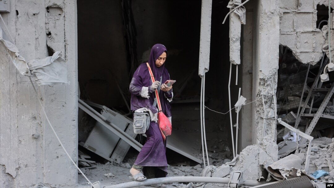 FILE - A woman checks her phone as she stands amid the rubble of a building destroyed during Israeli bombardment in Gaza City's Sheikh Radwan neighborhood, Aug. 11, 2024.