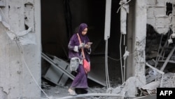 FILE - A woman checks her phone as she stands amid the rubble of a building destroyed during Israeli bombardment in Gaza City's Sheikh Radwan neighborhood, Aug. 11, 2024.