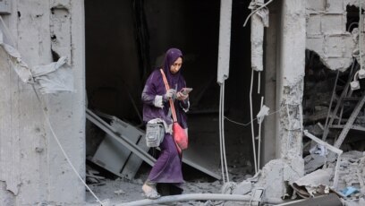 Una mujer revisa su teléfono mientras está de pie entre los escombros de un edificio destruido durante un bombardeo israelí en el barrio Sheikh Radwan de la ciudad de Gaza, el 11 de agosto de 2024.