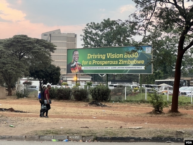 Citizens walk past a banner of President Emmerson Mnangagwa saying Zimbabwe is shaping to be prosperous by 2030 in Harare. (Columbus Mavhunga/VOA)