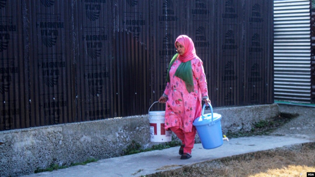 Kausar Jan, a cook at a local government primary school in the Dal Lake area, carries buckets of water to prepare the midday meals for children. (Muzamil Mattoo/VOA)