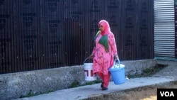 Kausar Jan, a cook at a local government primary school in the Dal Lake area, carries buckets of water to prepare the midday meals for children. (Muzamil Mattoo/VOA)