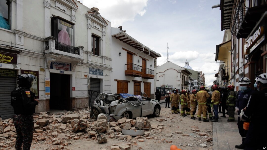 Rescue workers stand next to a car crushed by debris after an earthquake in Cuenca, Ecuador, March 18, 2023. The U.S. Geological Survey reported an earthquake with a magnitude of 6.7 about 50 miles south of Guayaquil. 