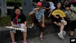 FILE - Tourists eat popsicles and fan themselves to cool off from the humid weather in Beijing, Aug. 9, 2023.