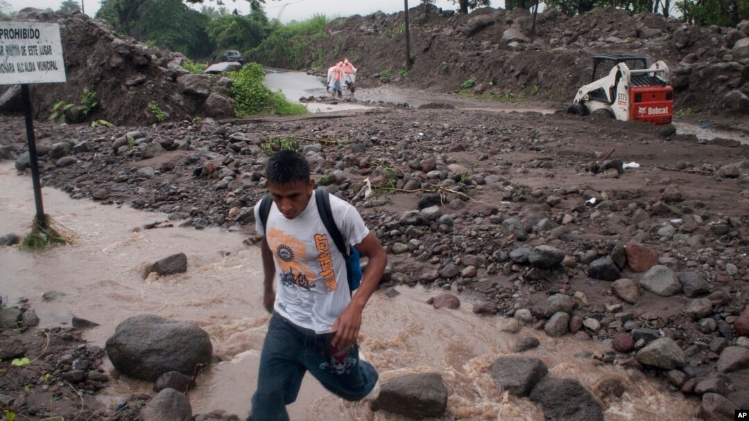 ARCHIVO - Un hombre cruza un arroyo en una carretera después de que un río se desbordó en Verapaz, El Salvador, el domingo 30 de mayo de 2010.