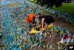 FILE - Tetiana Poltorak, left, and Tetiana Artemenko place flags to honor Ukrainian prisoners of war killed in the Olenivka region at a memorial site near the Independence Square in Kyiv, Ukraine, July 5, 2023.