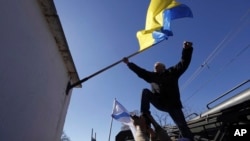 FILE - A man removes a Ukrainian flag after seizure of the base in Novofedorivka, Crimea, March 22, 2014.