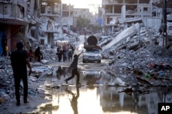 FILE - Palestinians displaced by the Israeli offensive in the Gaza Strip walk past sewage flowing into the streets of Khan Younis, July 4, 2024. Health authorities and aid agencies are racing to avert an outbreak of polio in the Gaza Strip.