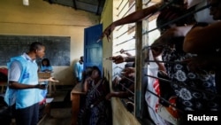 An election official checks the identity cards of people who are waiting to vote in the Democratic Republic of the Congo's parliamentary and presidential elections, in Kinshasa, Dec. 21, 2023. 