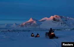 Para ilmuwan NPI (Norwegian Polar Institute) mengendarai mobil salju mereka saat matahari terbenam di tepi Kongsfjord dan gletser Kronebreen dekat Ny-Aalesund, Svalbard, Norwegia, 10 April 2023. (Lisi Niesner/REUTERS)