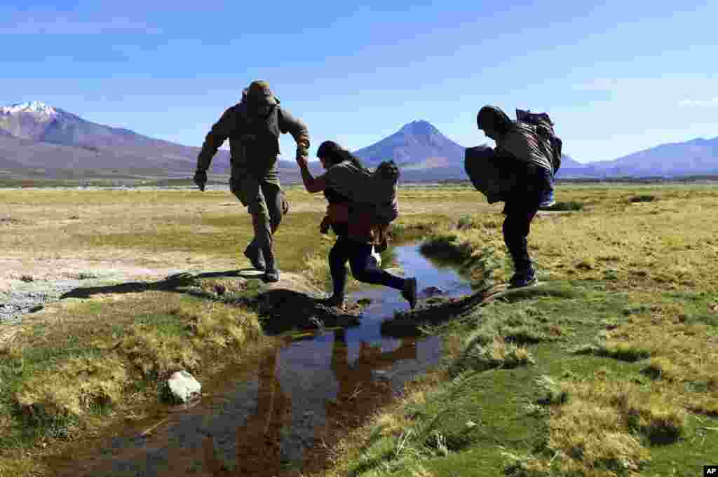 Чилеански војник му помага на мигрант да помине преку воден канал во близина на Колчане пред мигрантите да бидат одведени во засолниште на границата со Перу и Боливија.