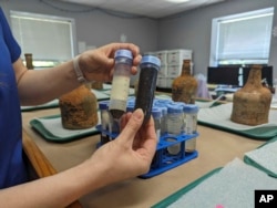 Curator Lily Carhart holds up different samples of liquid they extracted from 18th-century glass bottles that contained fruit after they were unearthed from the cellar of George Washington's residence in Mount Vernon, Va., Monday, June 17, 2024. (AP Photo/Nathan Ellgren)