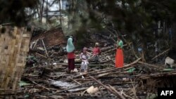 Sejumlah warga duduk dan berdiri di atas rumah mereka yang hancur di kamp pengungsi Basara di Sittwe pada 16 Mei 2023, setelah topan Mocha menghantam wilayah itu, 16 Mei 2023. (Foto: Sai Aung Main/AFP).