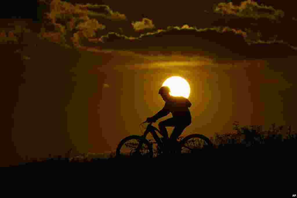A cyclist tops a hill at sunset Aug. 20, 2023, in San Antonio, where temperatures continue to hit the triple-digit mark.