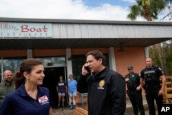 Florida Governor Ron DeSantis talks on the phone with U.S. President Joe Biden as he and wife Casey, left, stop at a storm-damaged restaurant during a visit to Horseshoe Beach, Fla., one day after the passage of Hurricane Idalia, on Aug. 31, 2023.