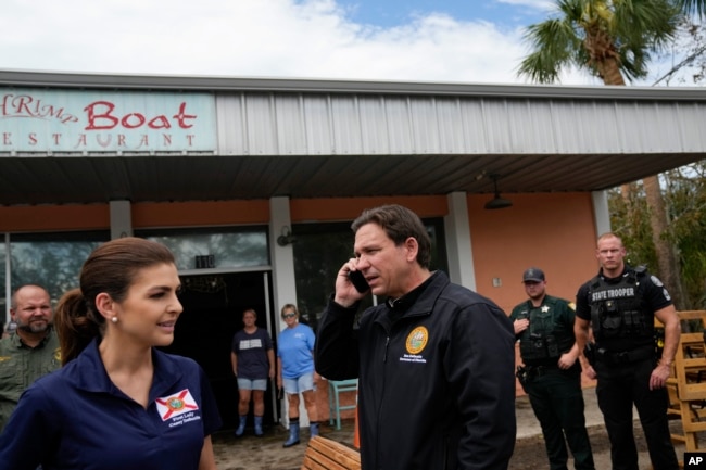 Florida Governor Ron DeSantis talks on the phone with U.S. President Joe Biden as he and wife Casey, left, stop at a storm-damaged restaurant during a visit to Horseshoe Beach, Florida, one day after Hurricane Idalia hit the state, Aug. 31, 2023.
