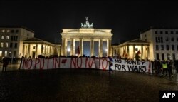 Spanduk bertuliskan 'No Putin, No Nato, No Money For Wars' digelar para aktivis di depan Gerbang Brandenburg di Berlin menandai peringatan setahun invasi Rusia di Ukraina, 23 Februari 2023. (Tobias SCHWARZ/ AFP)