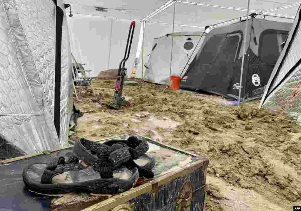 A pair of Teva sandals are seen on a chest in the middle of tents sitting in a muddy desert plain, Sept. 3, 2023. Tens of thousands of festivalgoers were stranded in deep mud in the Nevada desert after rain turned the annual Burning Man gathering into a quagmire.