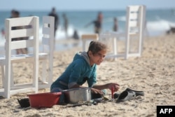 Palestinska devojčica pere posuđe na plaži u Deil al Balahu, u centralnom delu Pojasa Gaze, 24. maja 2024.