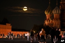 The August Super Blue Moon sets behind a historical building and the St. Basil's Cathedral, right, as people walk in Red Square in Moscow, Russia, Wednesday, Aug. 30, 2023. (AP Photo/Alexander Zemlianichenko)
