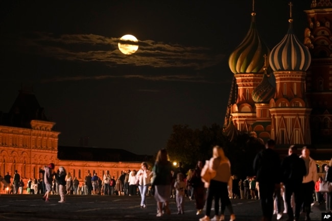 The August Super Blue Moon sets behind a historical building and the St. Basil's Cathedral, right, as people walk in Red Square in Moscow, Russia, Wednesday, Aug. 30, 2023. (AP Photo/Alexander Zemlianichenko)