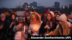 People lay flowers and light candles standing next to the Crocus City Hall, on the western edge of Moscow, Russia, March 23, 2024. (AP Photo/Alexander Zemlianichenko)