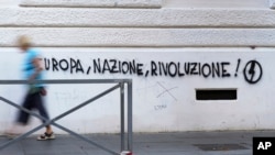 A woman walks past a mural by right-wing students movement named 'Blocco Studentesco' (Student Block) and reading: 'Europe, Nation, Revolution' in downtown Rome, Aug. 13, 2023.