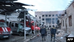 乌克兰救援人员走过乌东城市第聂伯河（Dnipro）一座被摧毁的救火站，救火站里停着几辆烧毁的紧急救援车辆。照片时间是2023年5月22号。