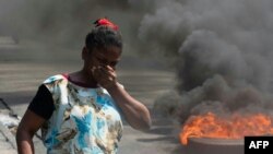 Seorang perempuan berjalan melewati ban yang dibakar dalam aksi demo di Port-au-Prince, menyusul pengunduran diri Perdana Menteri Haiti Ariel Henry, pada 12 Maret 2024. (Foto: AFP/Clarens Siffroy)