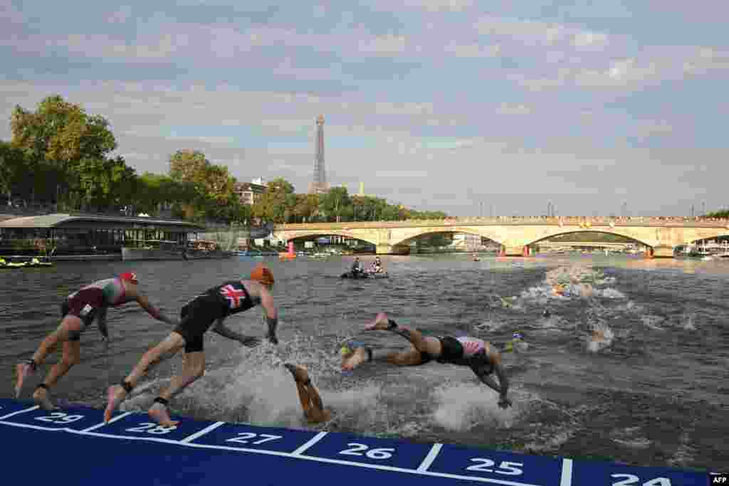 Triathletes dive into The Seine river with the Eiffel Tower in the background during the men's 2023 World Triathlon Olympic Games Test Event in Paris.