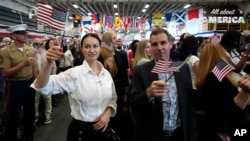New American citizens wave US flags during a naturalization ceremony aboard the USS Bataan on May 7, 2024, in Miami. 